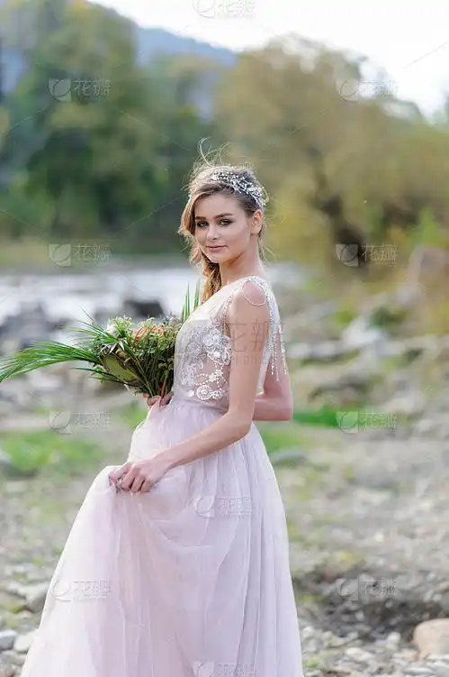穿着粉色婚纱的快乐新娘那个女孩手里拿着一束婚礼花束在河边举行波西米亚风格的婚礼婚礼